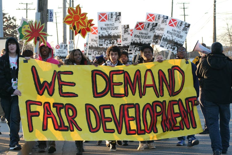 Protesters march behind a sign reading 'We demand fair development'.