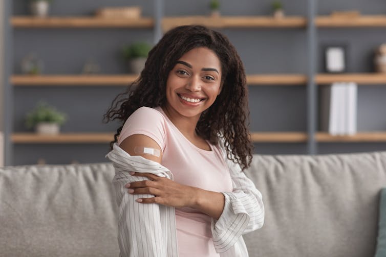 A young woman shows a bandaid on her upper arm.