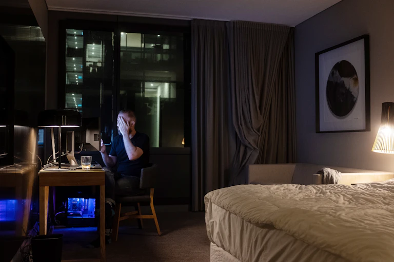 Man covers his face in hotel room at night.