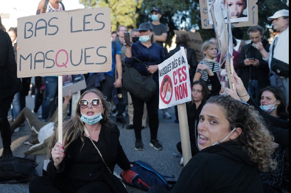 Plusieurs femmes tiennent des panneaux protestant contre le port obligatoire du masque.