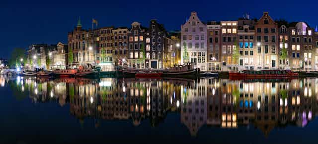 Buildings lit up against a night sky are reflected in the still waters of an Amsterdam canal