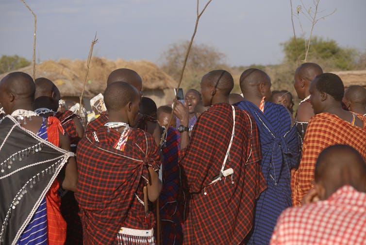 In a crowd of people in traditional Maasai dress, one man holds a mobile phone.