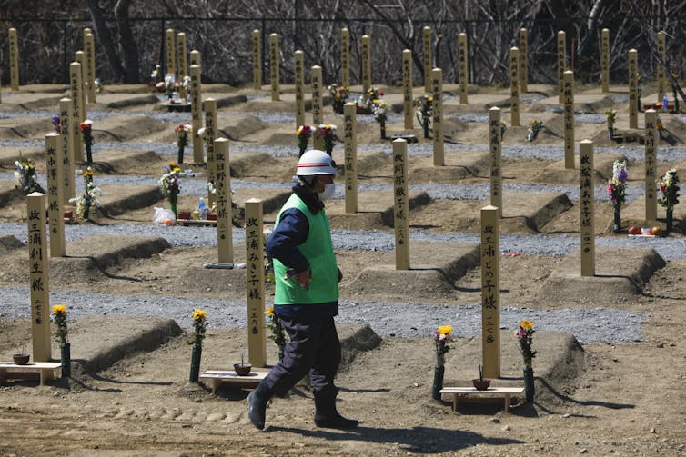 A man in green vest walks past makeshift graves.