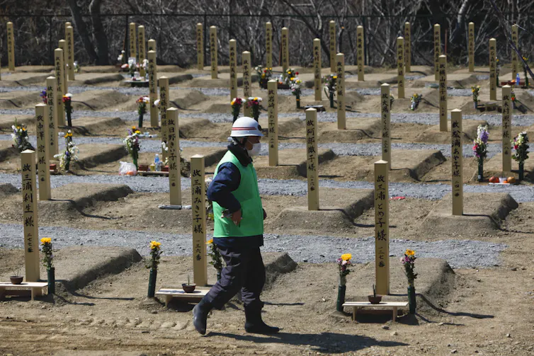 A man in green vest walks past makeshift graves.