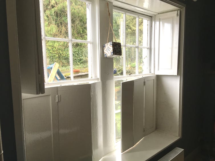 A white wooden window frame with attached shutters on the inside.