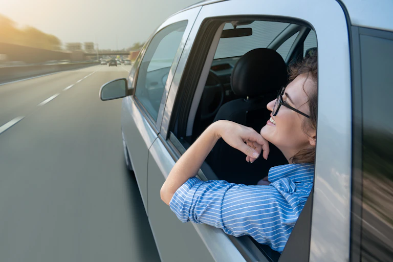 A woman sits in the back seat of a moving car, no driver is visible