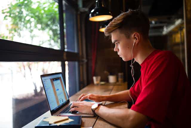 Student sits on his laptop with headphones in at a cafe bar table
