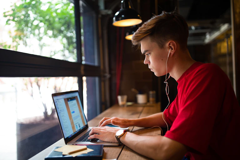 Student sits on his laptop with headphones in at a cafe bar table