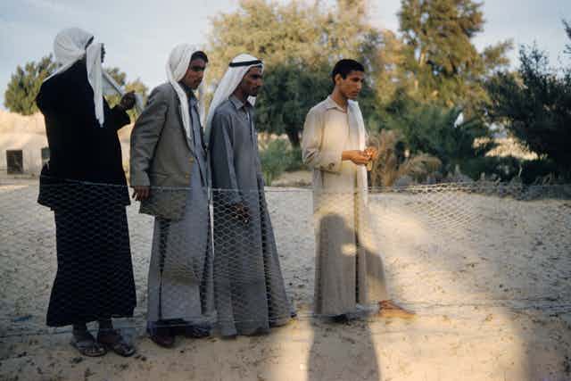 Quatre hommes debout en robes grises et beiges.