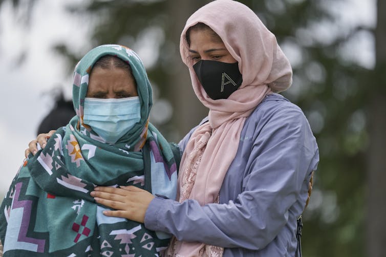 Two women wearing hijabs stand with their arms around each other.