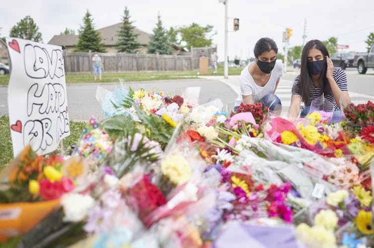 Two women lay flowers at a makeshift memorial on a sidewalk.