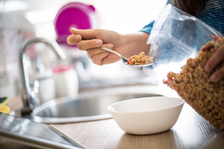 hand spoons cereal from a packet into bowl