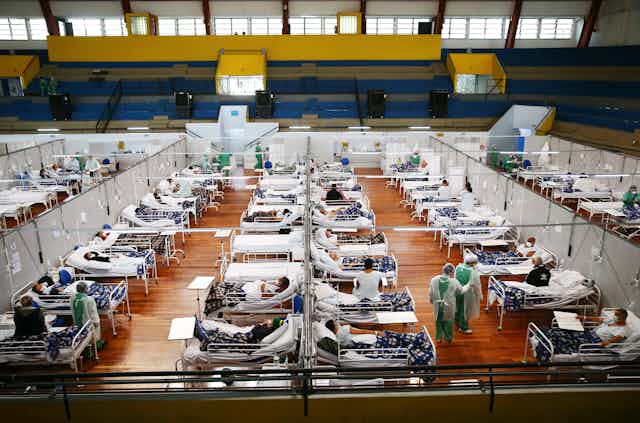 Aerial shot of dozens and dozens of beds with sick patients lined up in a gym
