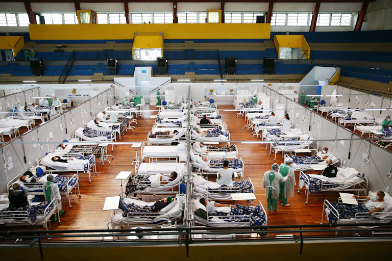Aerial shot of dozens and dozens of beds with sick patients lined up in a gym