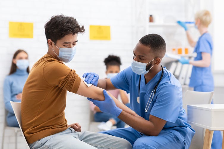 Una enfermera de color administra una vacuna a un hombre asiático