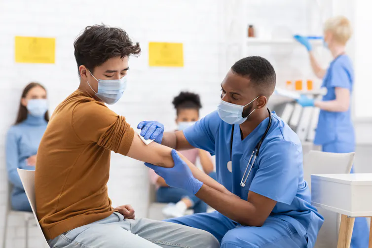 Black nurse adminsters a vaccine shot to Asian man