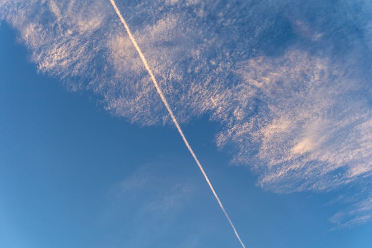 A blue sky with a contrail line and wispy cirrus clouds.