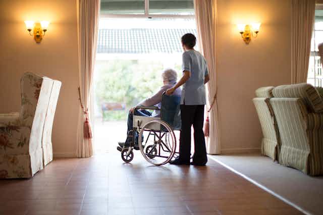 Elderly person in a wheelchair at a care home with a care home worker pushing the chair