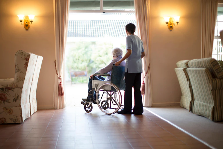 Elderly person in a wheelchair at a care home with a care home worker pushing the chair