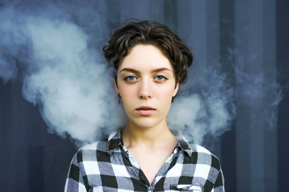 Young woman standing against a black background wreathed in smoke.