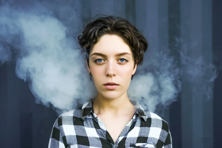 Young woman standing against a black background wreathed in smoke.