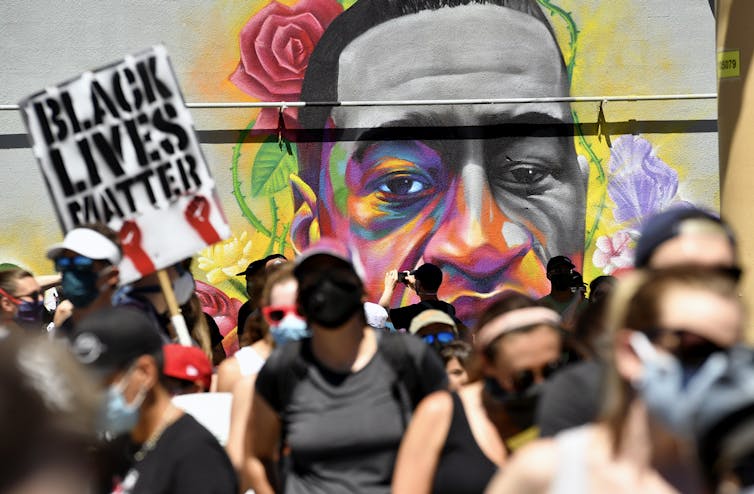 Marchers walk by a mural of George Floyd.