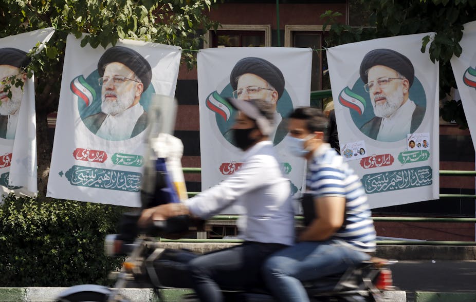 Two Iranian men on a motorcycle ride past election flags for conservative candidate Ebrahim Raisi, Tehran, June 2021.