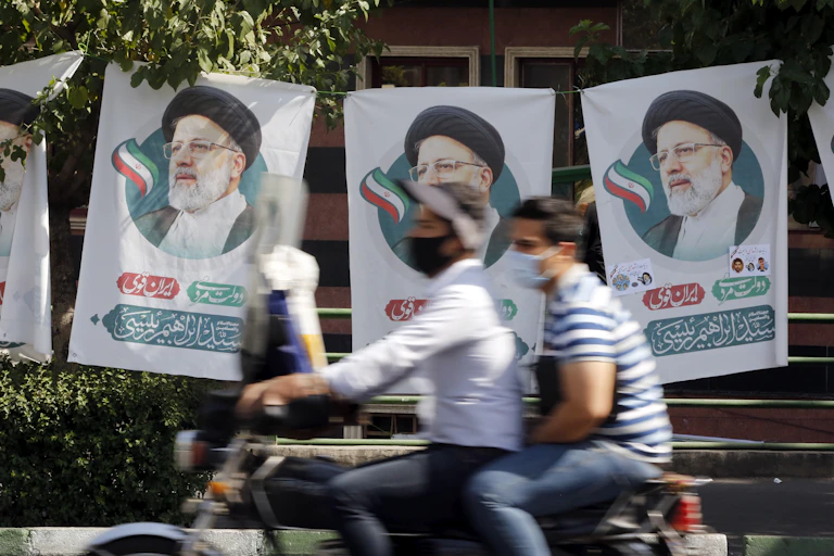 Two Iranian men on a motorcycle ride past election flags for conservative candidate Ebrahim Raisi, Tehran, June 2021.