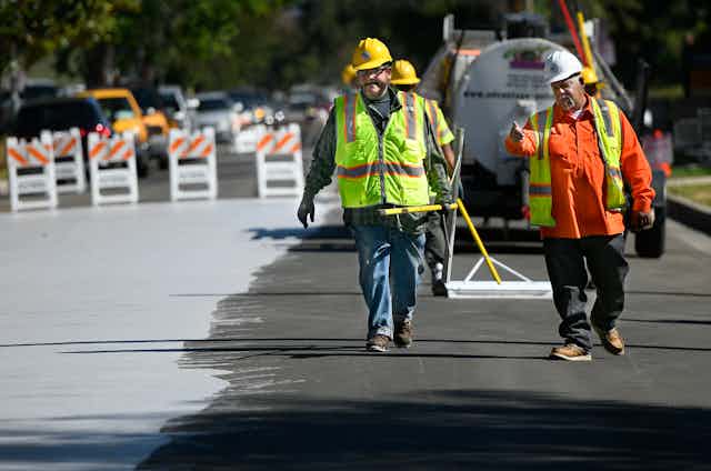 Workers spread light-colored coating on a roadway..