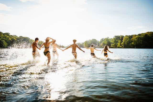 Groupe de personnes pataugeant dans un lac par une journée ensoleillée.