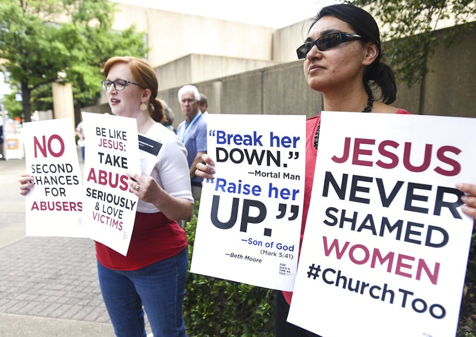 Two young women holding signs with slogans demanding action on church leaders' abuse of women and an end to shaming women victims of sexual abuse, outside a Southern Baptist Convention meeting in 2019.