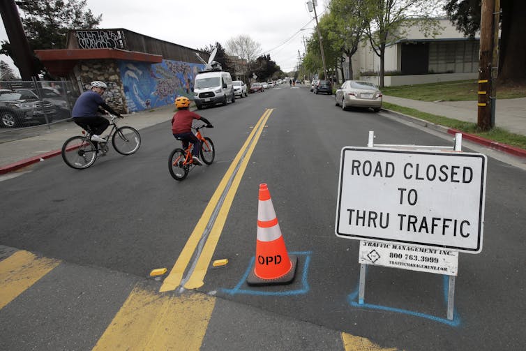 A man and child ride bikes past a street closure sign.