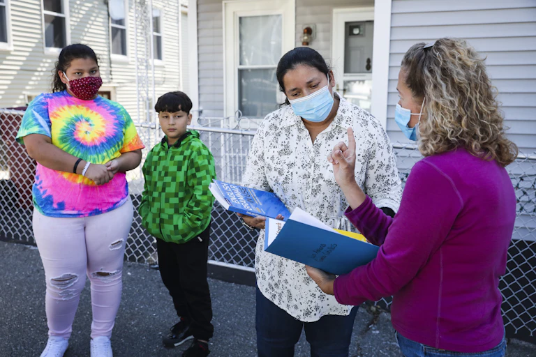 Mother talks with child's school teacher as her kids stand nearby