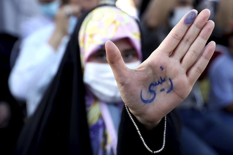 An Iranian woman holds out her hand, which has the name 'Raisi' on it written in Persian script