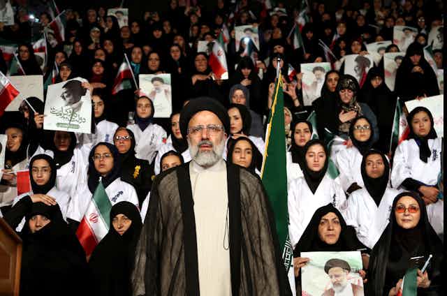 Ebrahim Raisi stands at a rally as supporters hold Iranian flags and pictures of him behind him