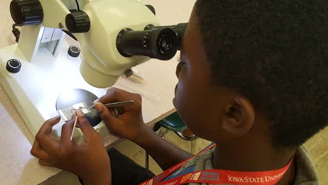 A young Black boy dissects a mosquito under a microscope.