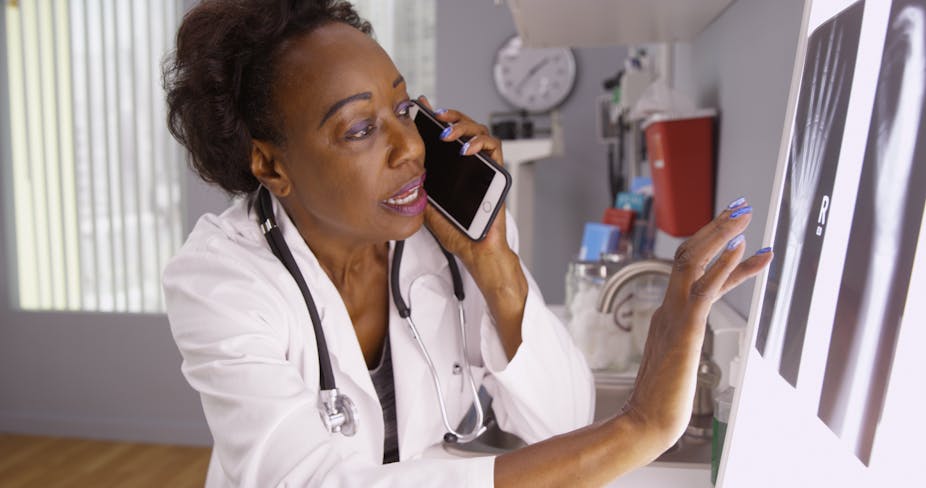 African female doctor communicating on phone with colleague while assessing x-ray images.