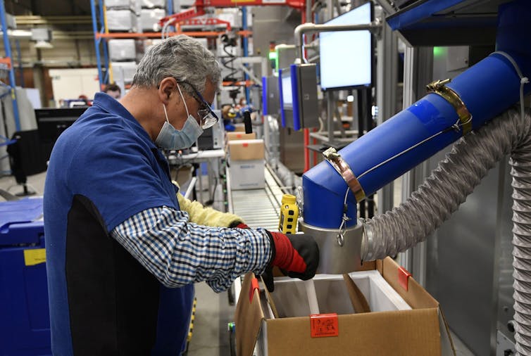 Man stands with mask working a machine at Pfizer vaccine factory in Belgium.