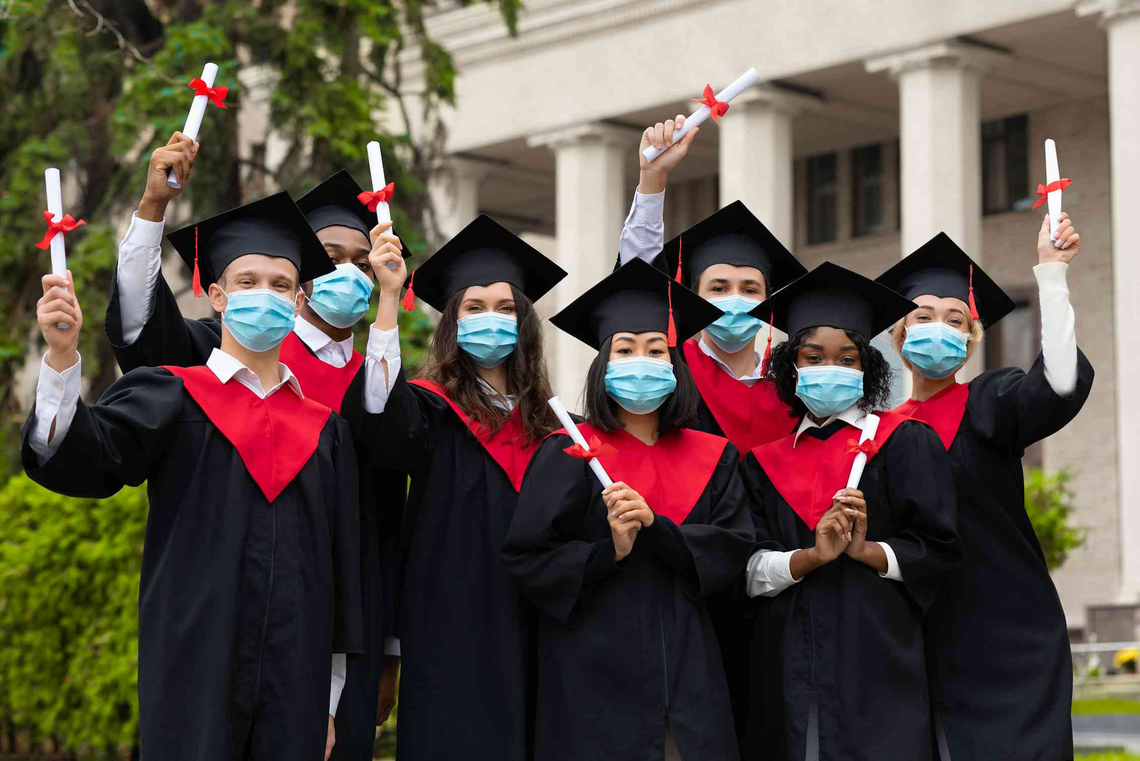 A group of graduates standing with diplomas wearing face masks.