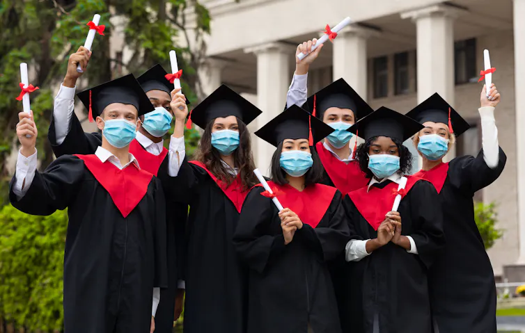 A group of graduates standing with diplomas wearing face masks.