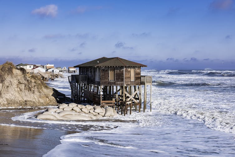 A storm-battered home on stilts in Nags Head sits out over the water with sandbags below it.