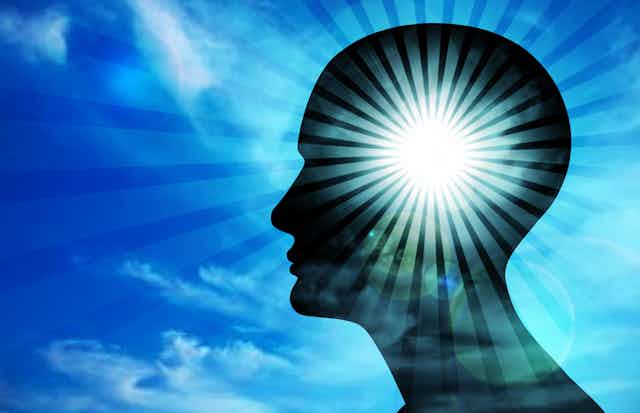 An illustration of a person's head in silhouette against a blue sky that is illuminated with a ray of light emanating outwards.