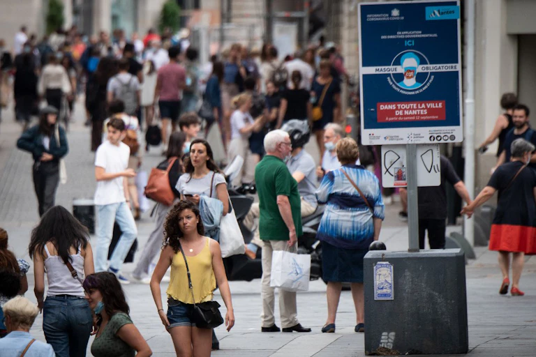 Photo d’une foule de passants sans masque, sous un panneau « masques obligatoires »