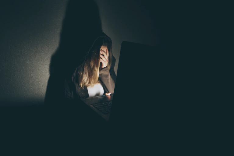 Mujer con la mano tapando el rostro ante un ordenador en penumbra.