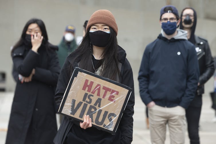 A woman holds a sign reading Hate is a Virus at a rally.