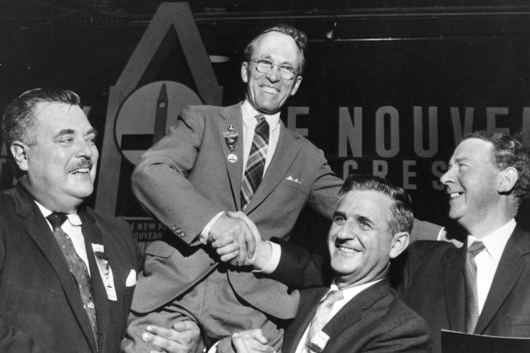 Tommy Douglas is held up by supporters in a black and white photo.
