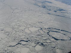 An aerial photo of pack ice with large block of ice floating on the sea and small cracks showing water between chunks of ice.