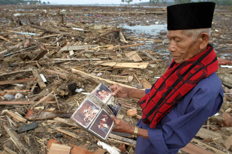A man looks at a photo album in a destroyed village.