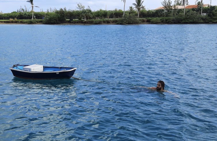 a man swimming near shore towing a small row boat