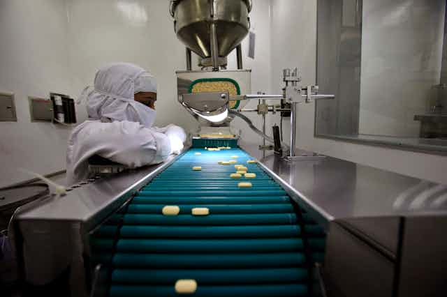 Pharmacist observing pills on a  conveyor belt in a lab.